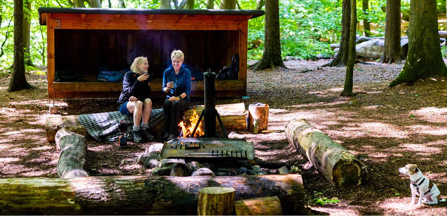 To kvinder ved bål foran shelter i Kollund Skov