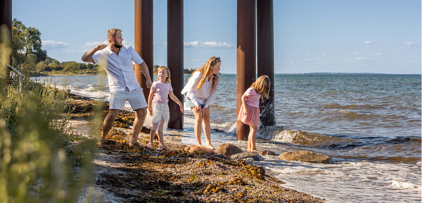 Familie står ved vandet en sommerdag og kaster sten