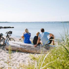 Family sitting next to their bikes on the beach and looking out over the water